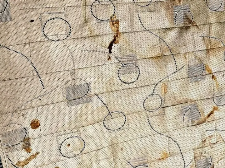 Colchão com várias manchas amareladas e escuras no tecido, antes da higienização